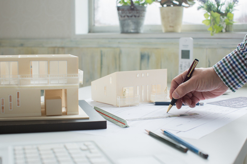 設計図を描いている手と家の模型を横から見た写真